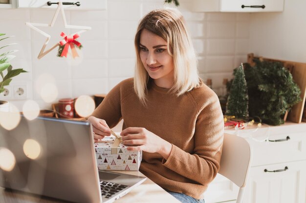 Attractive woman video chatting on laptop for christmas holidays and packing gifts