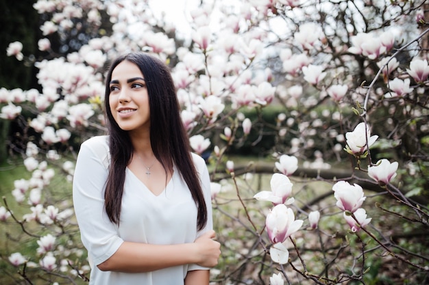 Attractive woman walks through the spring garden, enjoys the scent of flowering magnolia trees