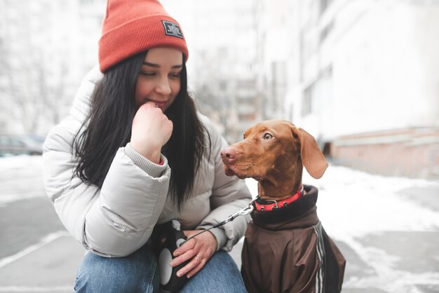 Attractive woman in warm clothes sitting on the street with a dog