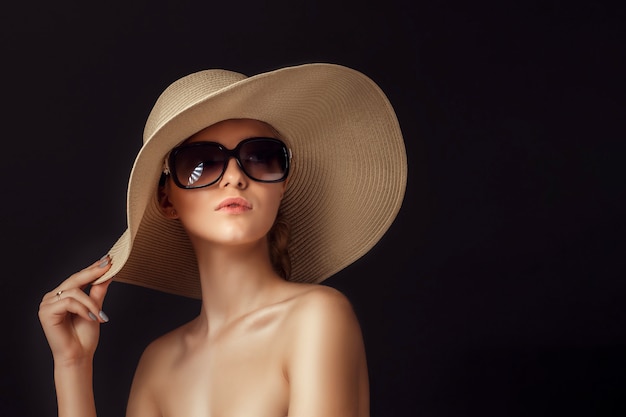 밀짚 모자와 포즈를 취하는 큰 선글라스를 착용하는 매력적인 여자