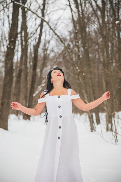 Attractive woman in white dress praying in the winter forest to higher powers