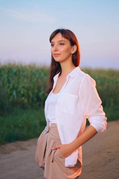 Donna attraente in camicia bianca che posa sulla strada campestre nel tramonto