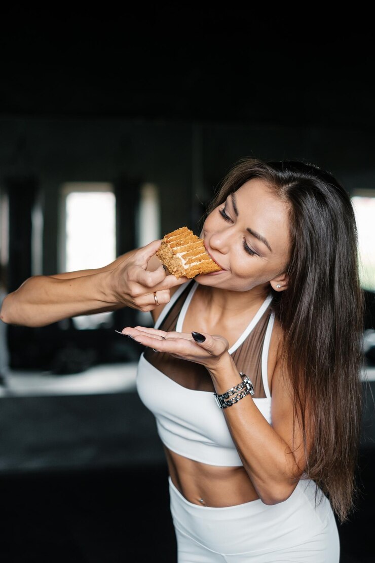 白いスポーツウェアの魅力的な女性はおいしいデザートを食べていますジムでトレーニングをしているセクシーな女の子ダイエットとフィットネスのコンセプト