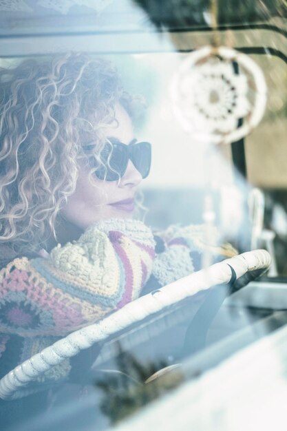 Attractive woman with blond curly hair looks out the window of her van spring nature and travel smiling excited about adventure and hipster lifestyle
