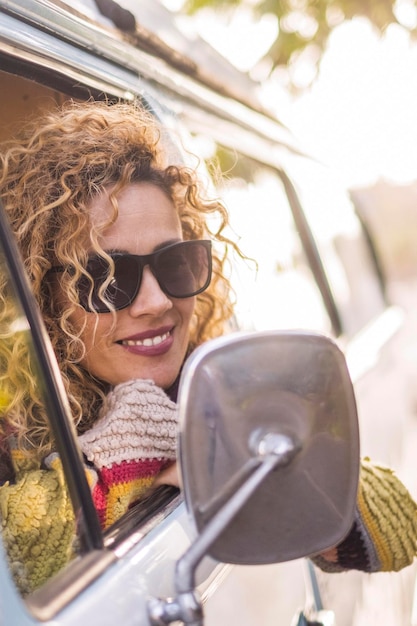 Attractive woman with blond curly hair looks out the window of her van spring nature and travel smiling excited about adventure and hipster lifestyle