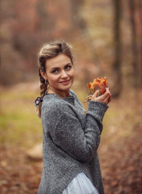 Attractive woman with braided pigtails holds fallen leaves