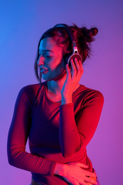 Attractive woman with headphones listening music in studio with blue and red lights