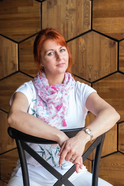 Attractive woman with red hair sits on a chair The woman is looking at the camera