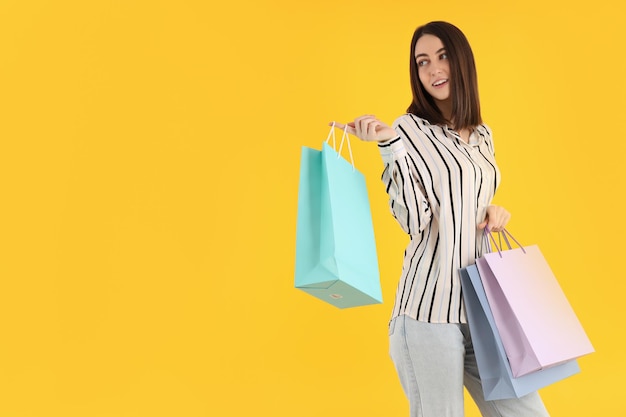 Attractive woman with shop bags on yellow background