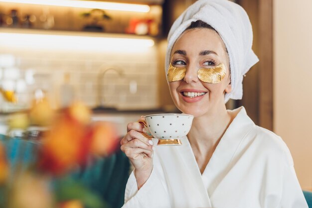 An attractive woman with skincare under eye patches enjoying morning coffee at her home.