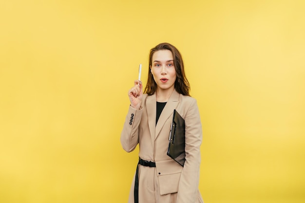 An attractive woman with a tablet and in a beige suit stands on a yellow background