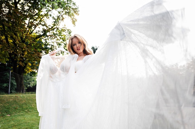 Attractive woman with trendy hairstyle and makeup holding on hanger her wedding dress while standing outdoors Concept of bride's morning