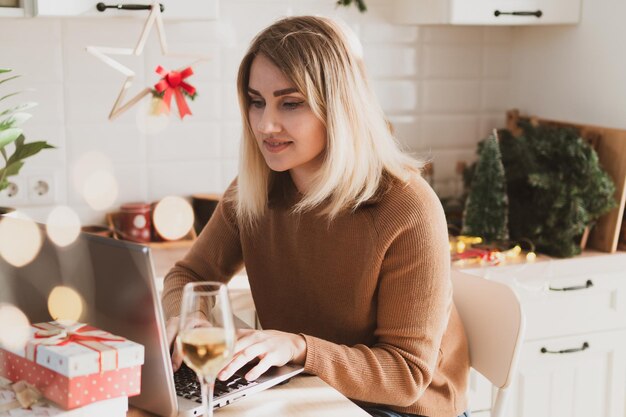 Donna attraente che lavora a distanza da casa sul laptop mentre è seduta nella sua cucina in cristo festivo