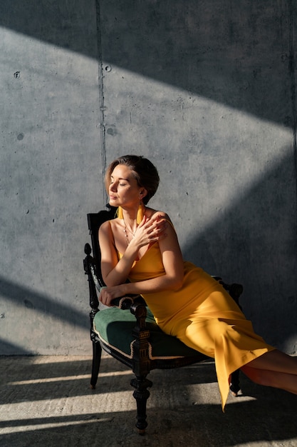 Attractive woman in yellow summer dress with short hairstyle in interior room concrete wall background posing, sunny shadows