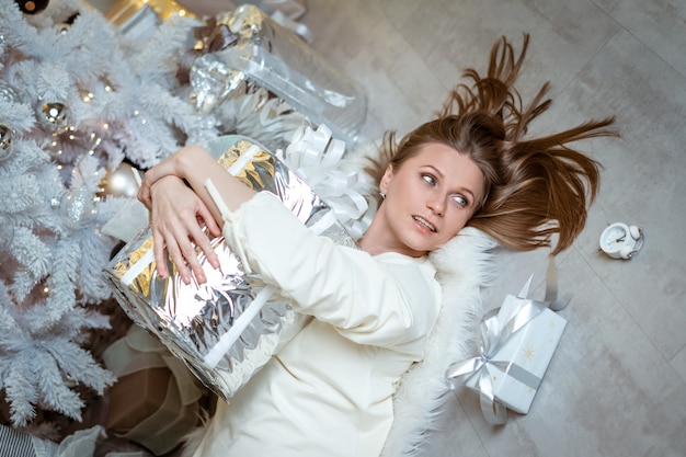 An attractive young adult woman blonde in a white dress is holding a gift in a silver package a woma...