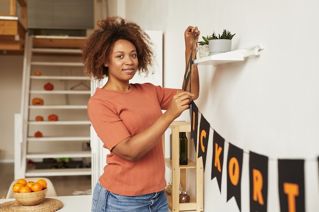 Attraente giovane donna afro-americana che decora la stanza con la ghirlanda per la festa di halloween, copia dello spazio