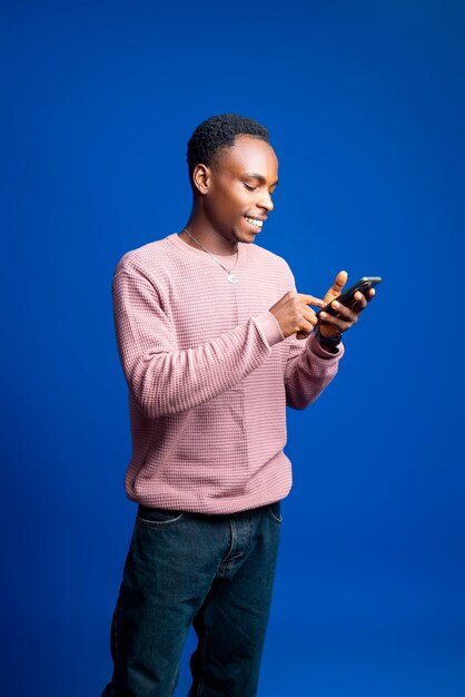 매력적인 젊은 아프리카 남자가 스마트폰을 사용하여 친구들과 연락하고 있습니다.