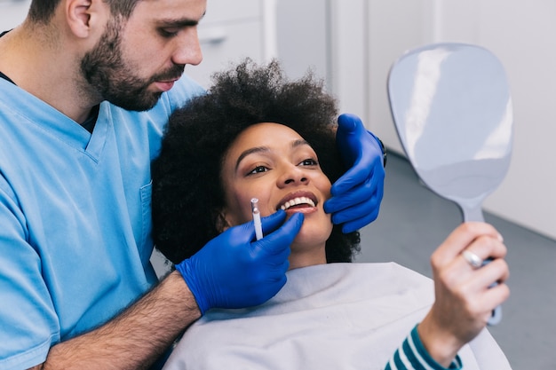 Attractive young African woman is getting a rejuvenating facial injections. She is sitting calmly at clinic. The expert beautician is filling female wrinkles by hyaluronic acid.