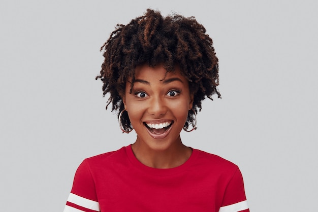 Attractive young African woman looking at camera and smiling while standing against grey background