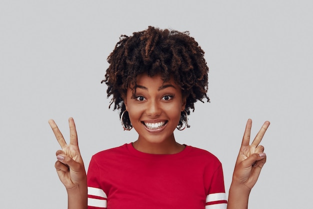 Attractive young African woman looking at camera with smile and gesturing while standing against grey background