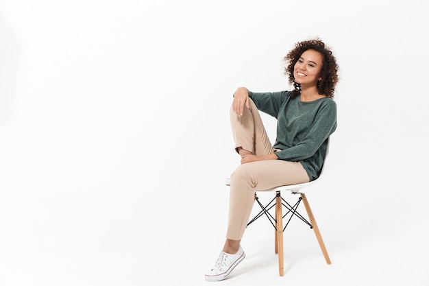 Photo attractive young african woman sitting on a chair isolated over white wall, posing