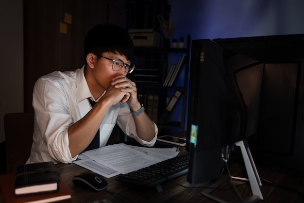 Привлекательный молодой азиатский бизнесмен сосредоточенно работает допоздна