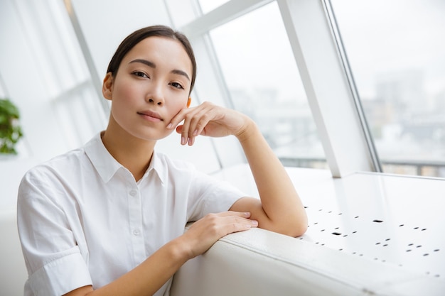 Attractive young asian businesswoman leaning on a couch while sitting at the cafe indoors