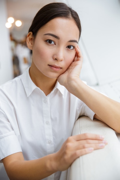 Attractive young asian businesswoman leaning on a couch while sitting at the cafe indoors