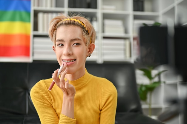An attractive young Asian gay beauty blogger applying lipstick to his lip talking to the camera