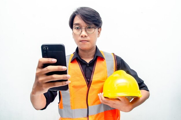 attractive young asian male construction worker in safety helmet and vest holding phone