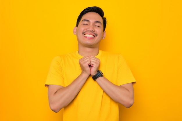 Attractive young Asian man in casual tshirt standing with closed eyes dreaming about future isolated on yellow background People lifestyle concept