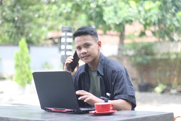 Photo attractive young asian man using laptop in coworking space with happy face and calling her friend