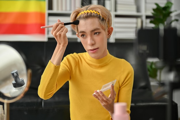 An attractive young Asian queer male beauty blogger is applying makeup contouring