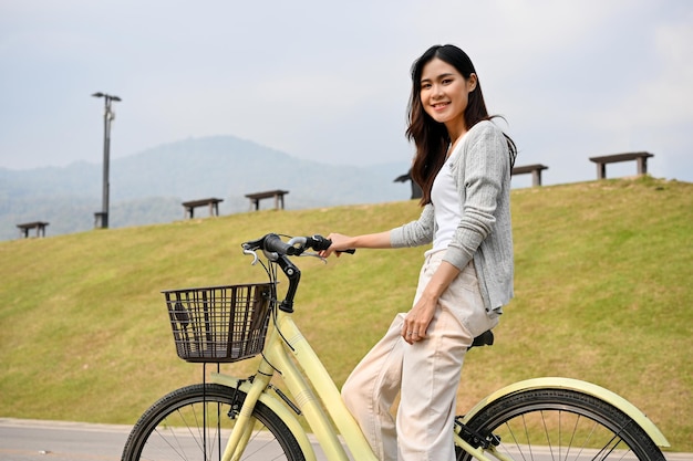 Привлекательная молодая азиатка на велосипеде улыбается и смотрит в камеру