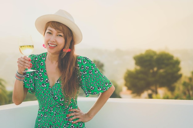 Attraente giovane donna asiatica che beve vino bianco su terrazza in stile vintage