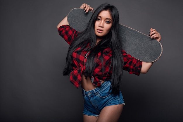 Привлекательная молодая азиатская женщина в фанк одежде со скейтбордом
