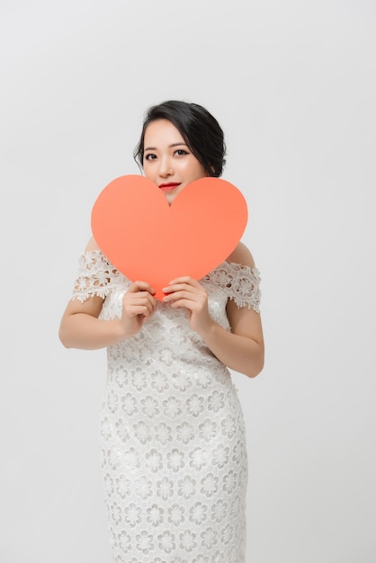 Attractive young Asian woman holding red love shape and standing over white background