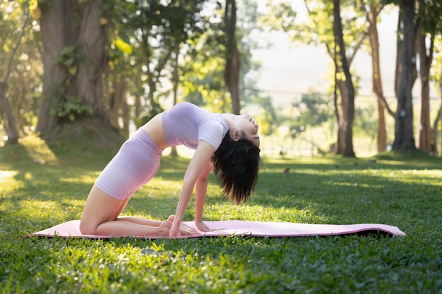 Привлекательная молодая азиатская женщина занимается йогой в парке, стоя одной ногой на коврике для йоги, демонстрируя равновесие, образ жизни и концепция деятельности