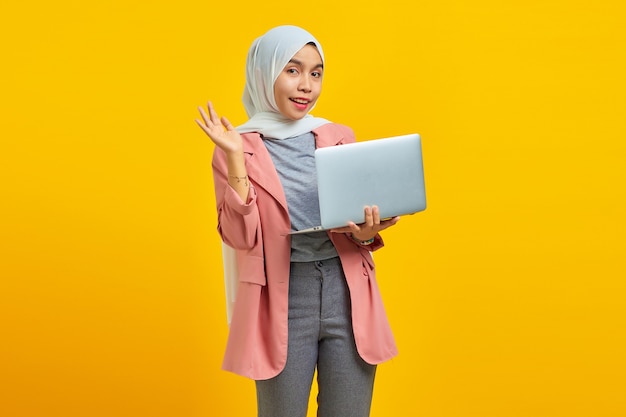 Attractive young asian woman smiling holding laptop and greeting