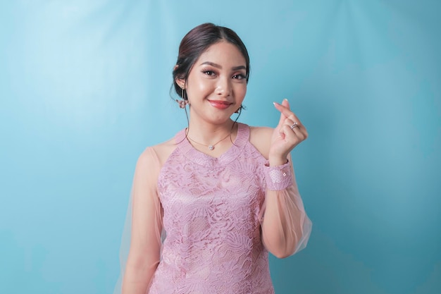 An attractive young Asian woman wearing a modern kebaya feels happy and a romantic shapes heart gesture expresses tender feelings