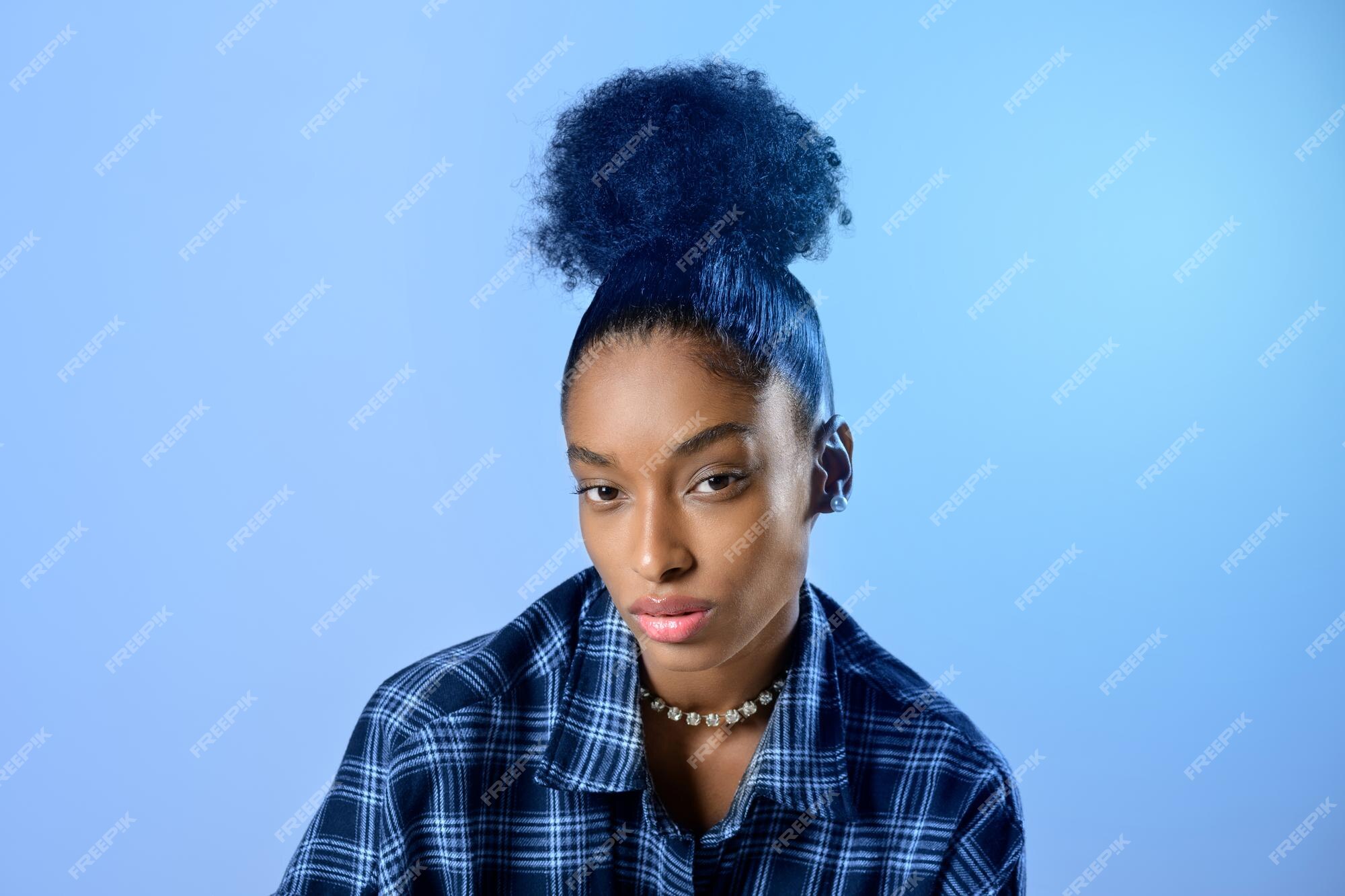Premium Photo | Attractive young black woman with her curly hair tied on  top of her head in a bun over a blue background