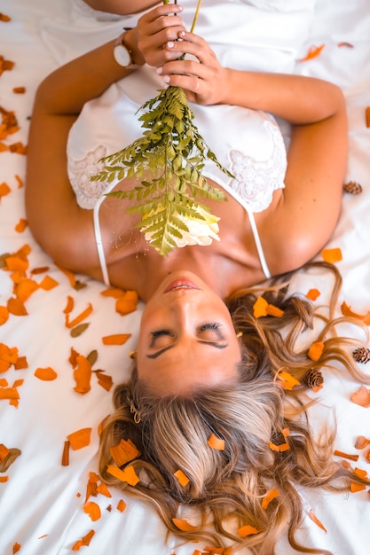 Foto attraente giovane donna caucasica bionda in camicia da notte nel letto dell'hotel pieno di petali di fiori, romantica notte d'albergo