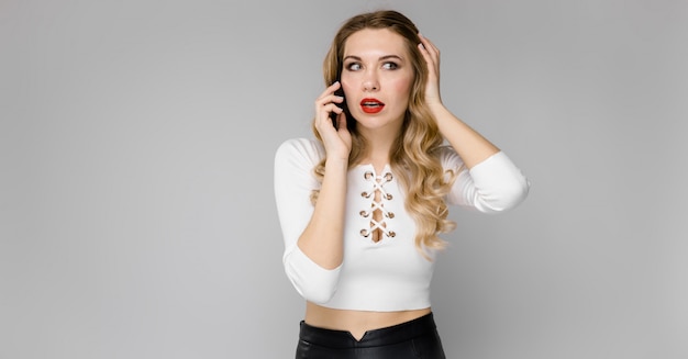 Фото Привлекательная молодая блондинка возбужденных деловая женщина в черно-белой одежде, улыбаясь, разговаривает по телефону, стоя в офисе