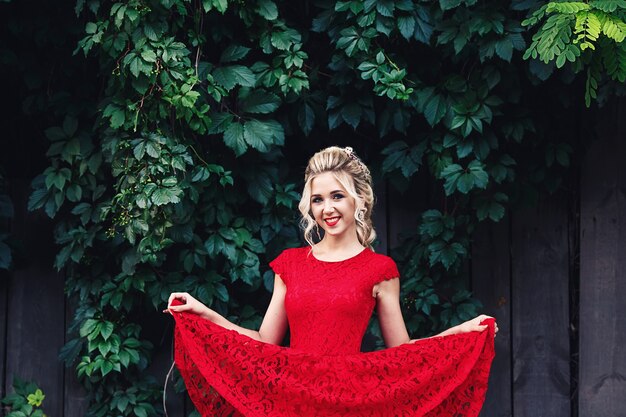 Attractive young blonde girl in red dress posing near a wild vineyard.