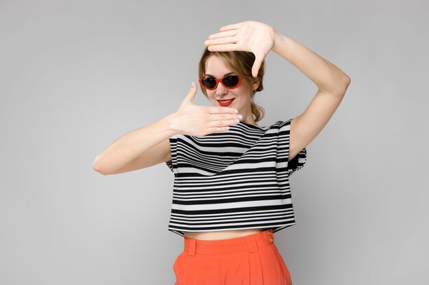 Attractive young blonde girl in striped blouse smiling in sunglasses standing  gray  