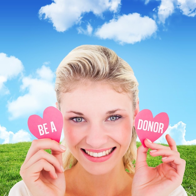 Attractive young blonde holding little hearts  against blue sky over green field