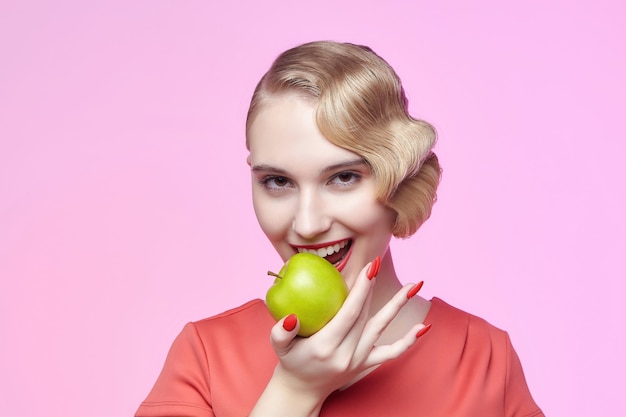 Photo attractive young blonde with a retro hairstyle is about to bite off a green apple