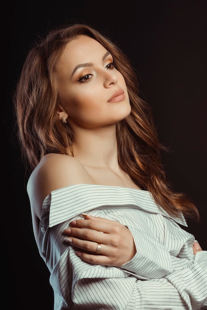 Attractive young brunette woman posing in men's shirt at studio