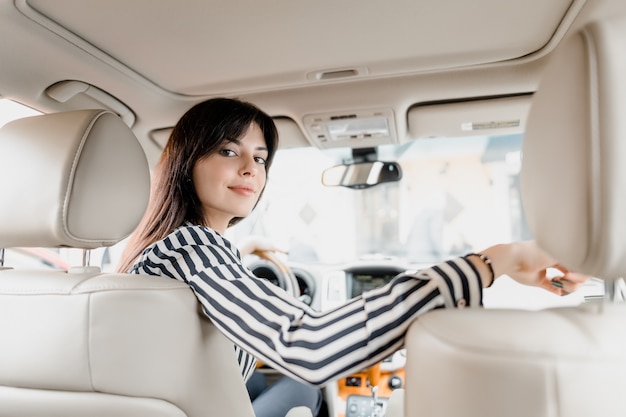 Фото Привлекательная молодая брюнетка женщина сидит за рулем автомобиля сидит и улыбается, глядя на заднее сиденье, где сидят ее дети