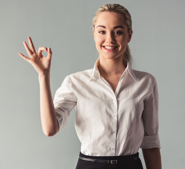 Attractive young business lady in suit is showing Ok sign.